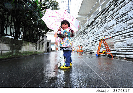 子供 傘 振り向く 水たまりの写真素材