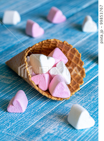 White and pink heart-shaped marshmallows are scattered from a cup