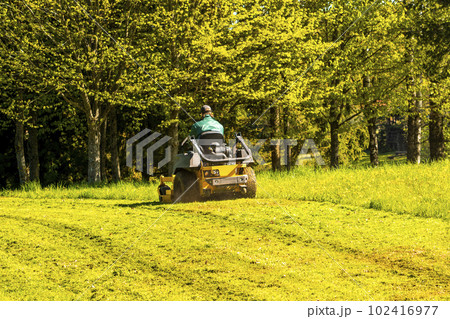 A Young White Man in a Straw Hat is Mowing a Lawn with a Lawn